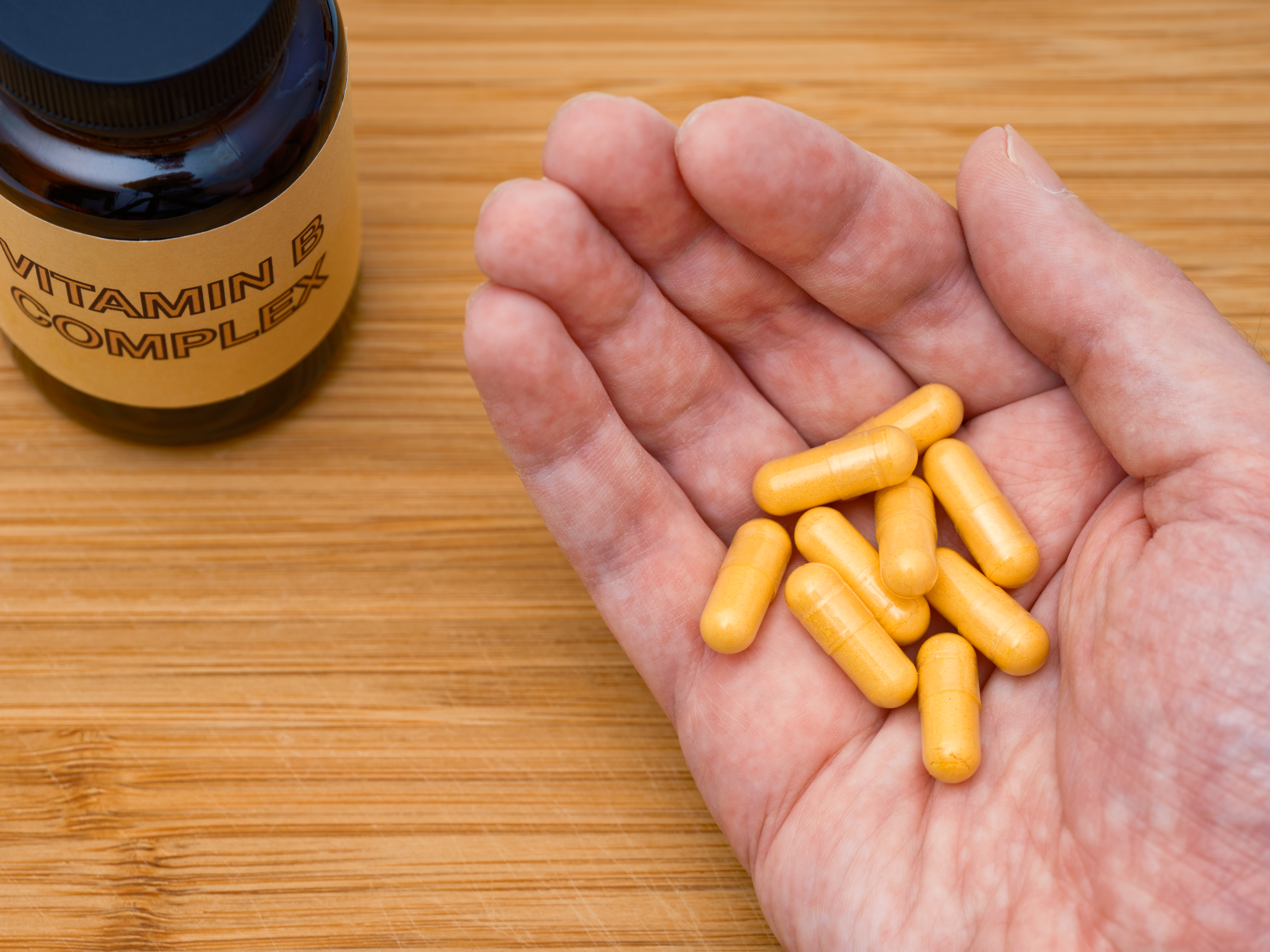 A man holding vitamin B Complex pills in his palm