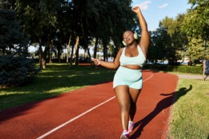 An African American woman in sportswear runs confidently along a red track outdoors, embodying body positivity and strength.