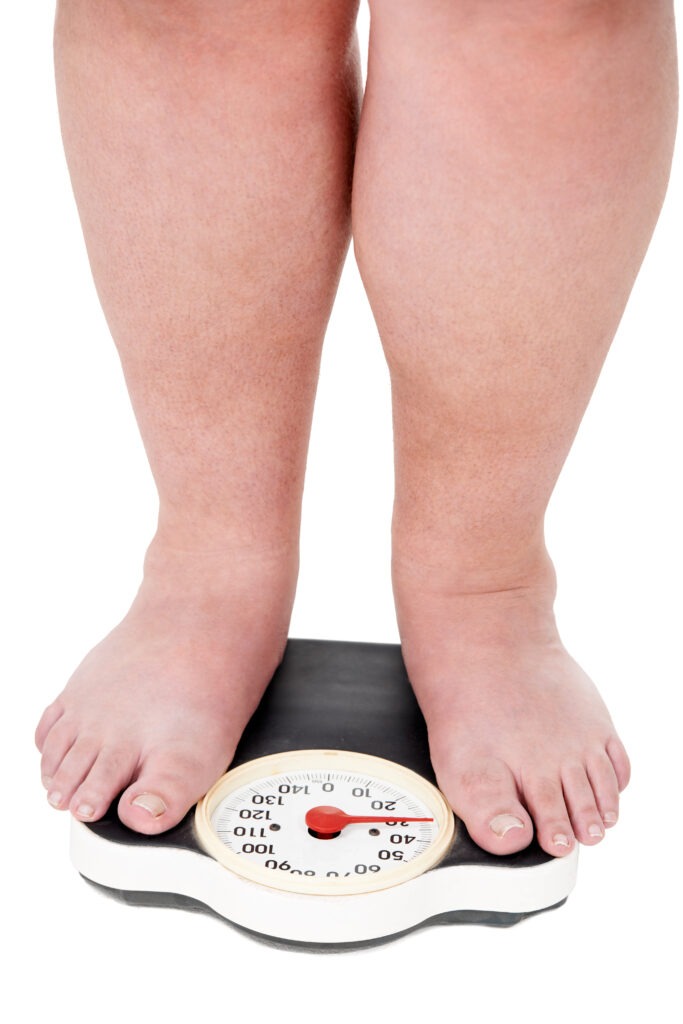 Another pound. A closeup shot of an overweight man weighing himself on a scale