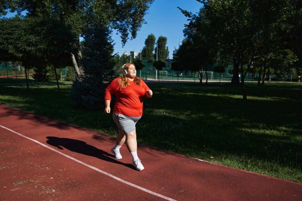 A plus size woman jogs with enthusiasm along a park path.