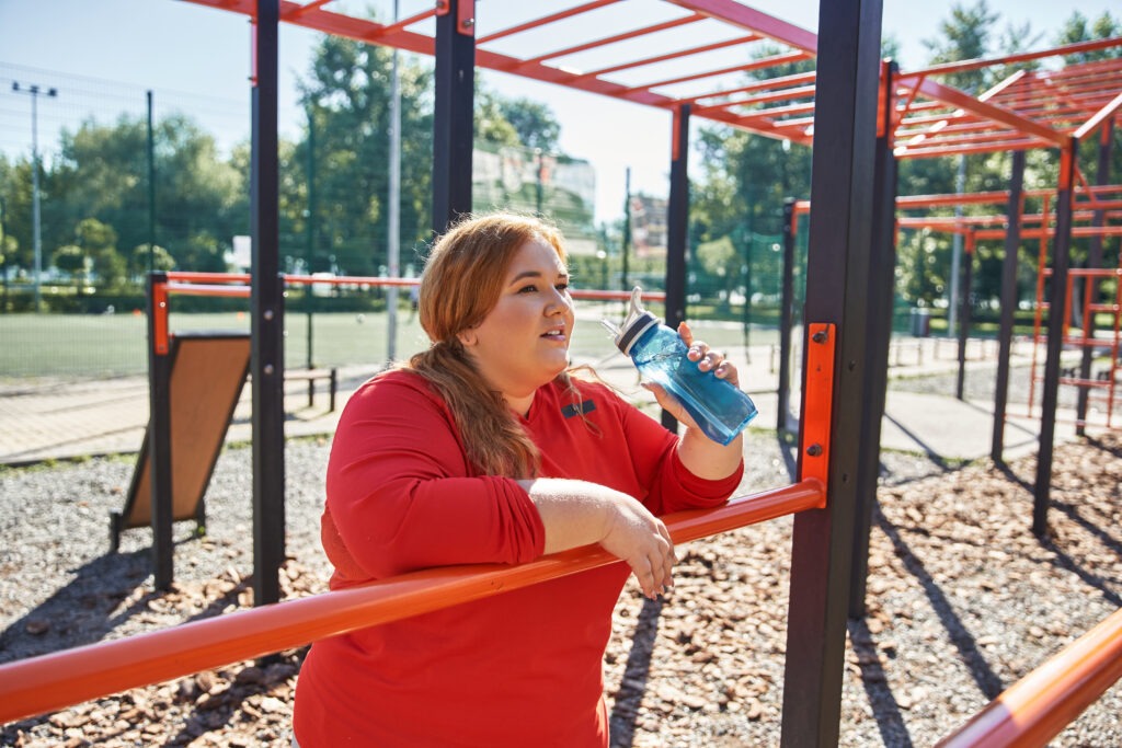 A cheerful woman takes a break to hydrate during her outdoor workout.