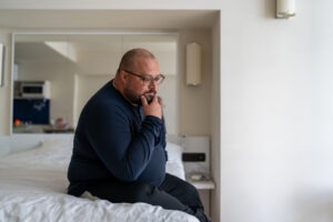 Sad confused depressed man sitting in bed at home and worrying about life troubles. Male terrified bad news feeling frustration, anxiety having problems. Thoughtful stressful overweight bearded guy.