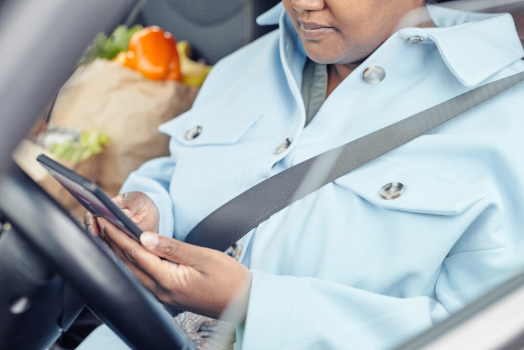 Close up of young black woman using smartphone in car with focus on safety belt