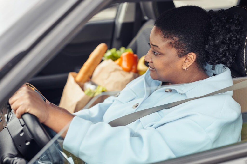 Side view portrait of black woman driving car with seatbelt on after shopping for groceries, copy space