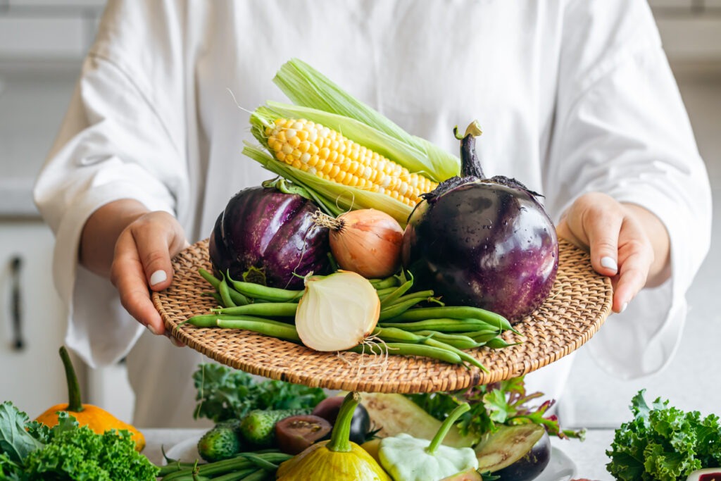 A woman holds a plate with eggplant, onion, corn and green beans, close-up.