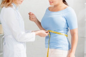 cropped view of nutritionist measuring body of patient with measuring tape in clinic