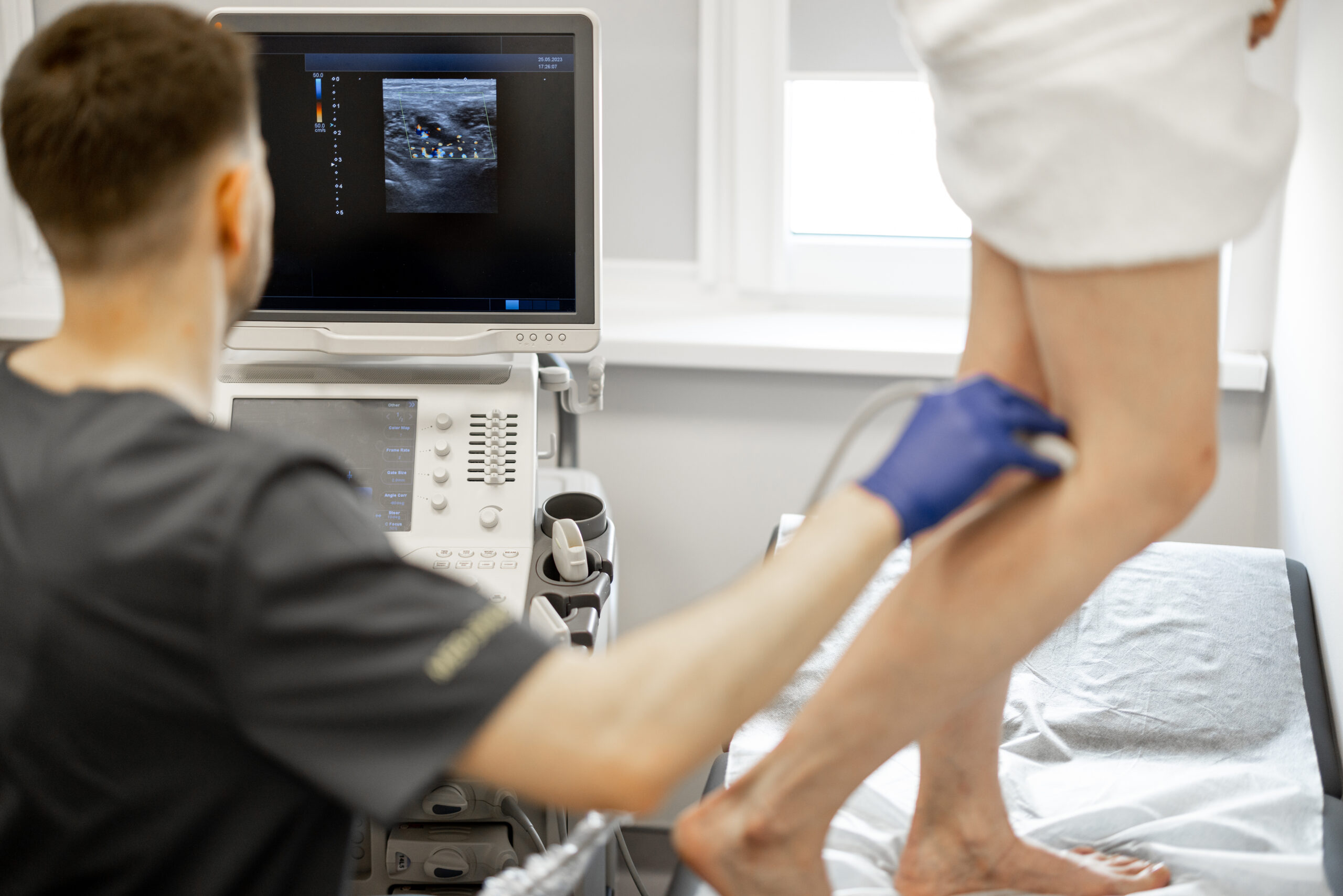 Ultrasound specialist is scanning the veins on a woman's leg, examining veins for varicose treatment